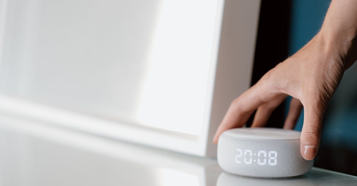 Close-up of a hand adjusting a smart speaker displaying time indoors.