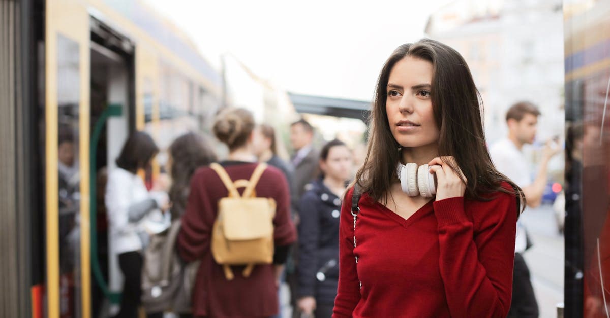 Woman with headphones at a busy train station in casual red attire.