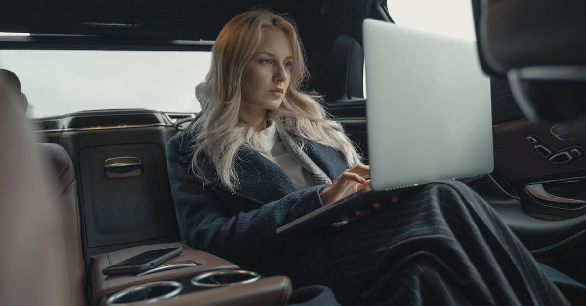 Businesswoman working on her laptop in the back seat of a luxury car.