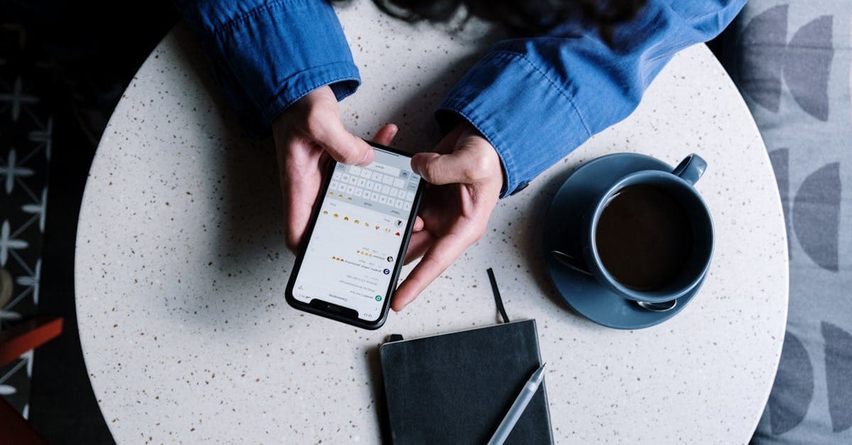 Person using smartphone at table with notebook and coffee, ideal for tech and lifestyle themes.