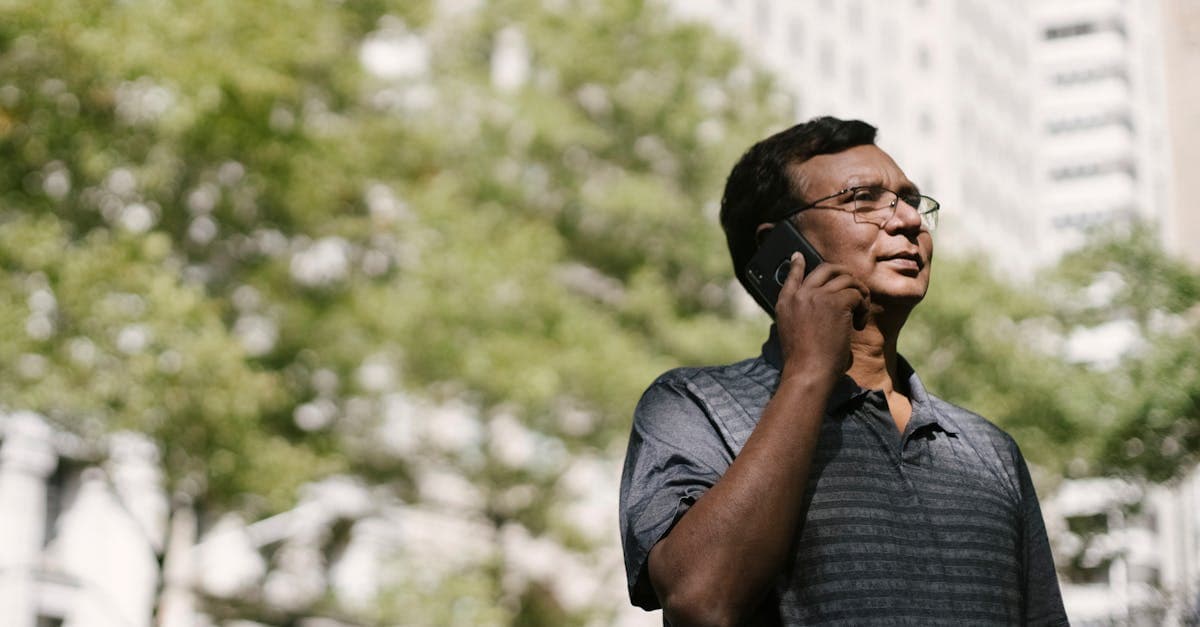 From below of ethnic man in casual clothes looking away talking on phone while standing on blurred background of street