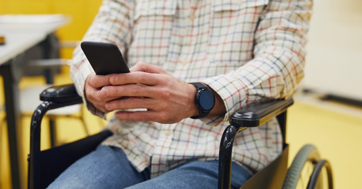 Adult using smartphone while seated in a wheelchair, wearing plaid shirt indoors.