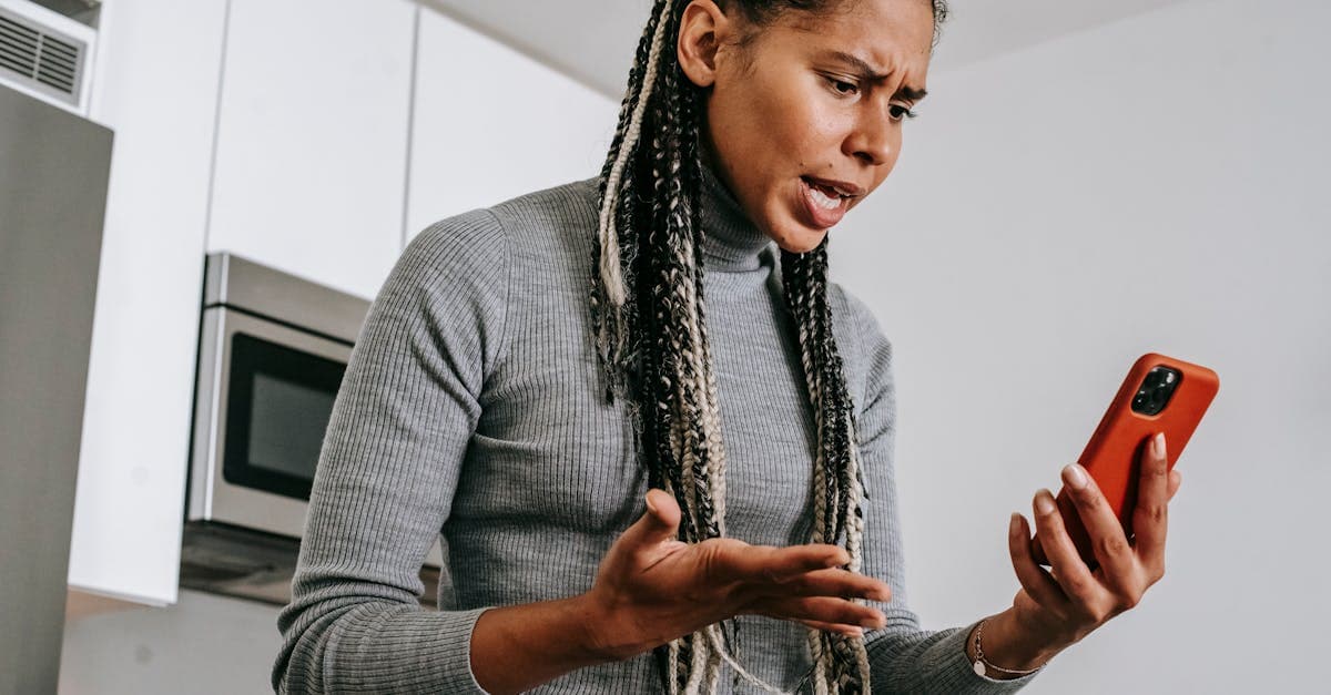 From below of angered black female with Afro braids in casual outfit gesticulating and resenting while having video call on smartphone in modern light kitchen