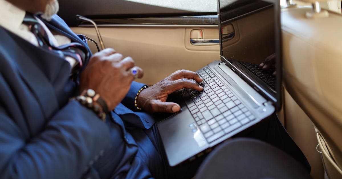 Close-up of a businessman typing on a laptop in a car interior during travel.
