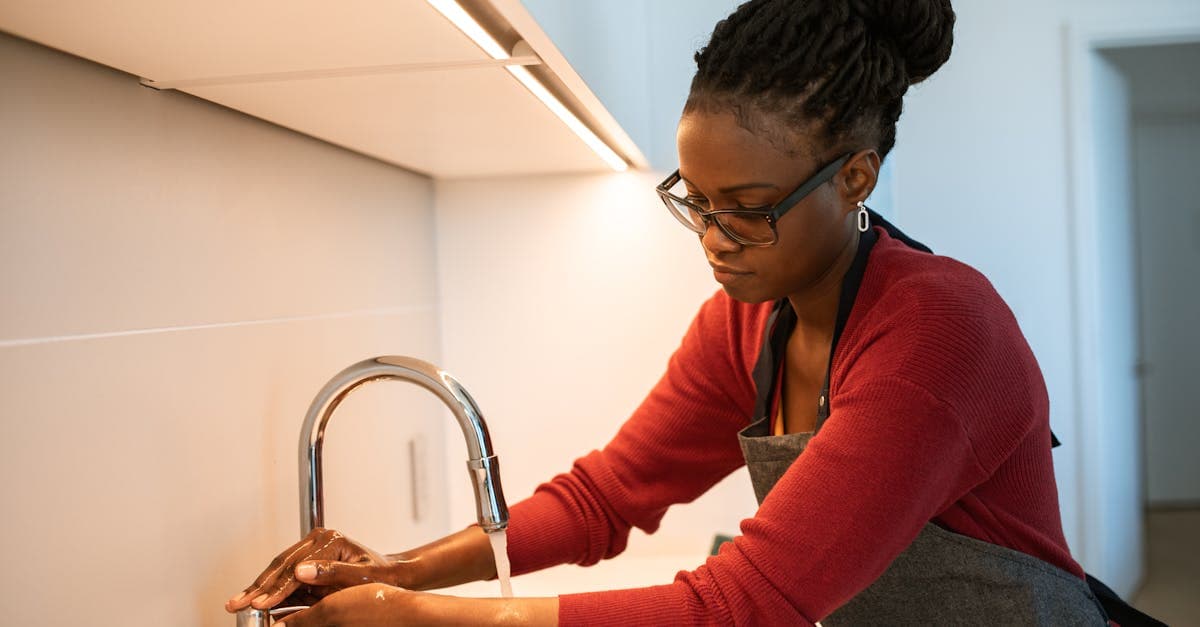 An adult woman with dreadlocks washing hands at a kitchen sink, emphasizing hygiene and cleanliness.