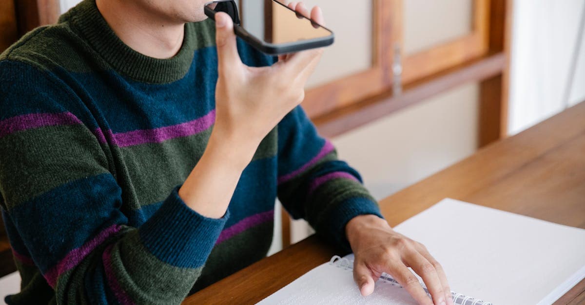 Adult man using smartphone for voice commands, smiling at home desk.