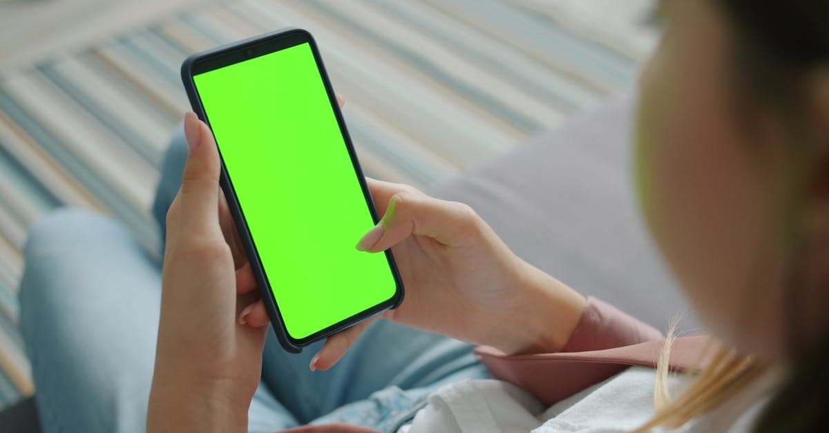Close-up of person holding smartphone with green screen indoors, for digital overlay.