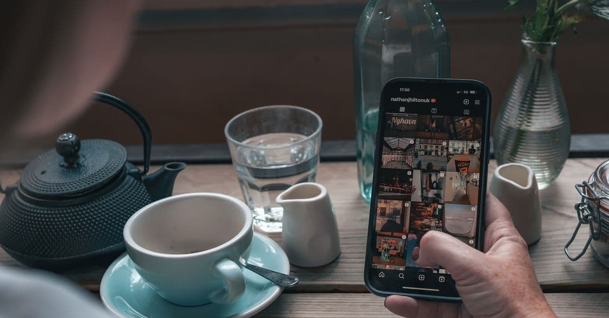 A person browsing Instagram on a smartphone in a cozy Manchester café setting with tea and glassware.