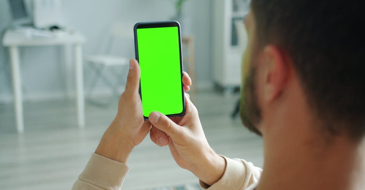 Man holding smartphone with green screen for mockup application indoors.