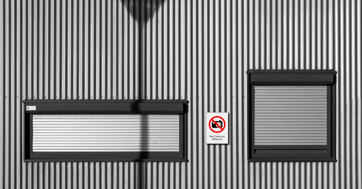 Corrugated metal wall with windows and a no camera sign casting shadows. Urban minimalism.